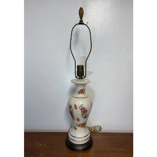 Vintage mid-century porcelain table lamp with colorful floral decoration, white body, and brass-tone base. Classic...