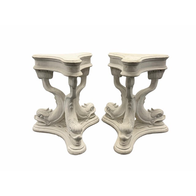 Striking pair of vintage Neoclassical pedestal bases with sculptural dolphin and scrolling motifs. Each base features a...