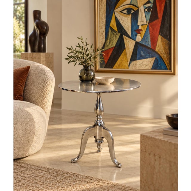A distinctive aluminum accent table with a polished oval top, turned pedestal, and three curved feet. The top and pedestal...