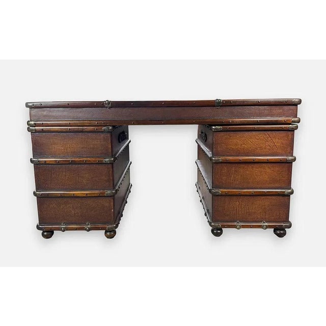 A striking campaign-style kneehole desk designed to evoke stacked vintage luggage. The distressed brown finish is accented...