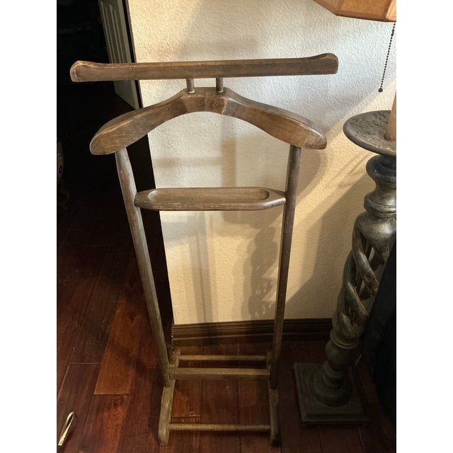 Classic vintage wooden valet stand featuring a sculpted jacket hanger, integrated trouser bar, and sturdy freestanding...