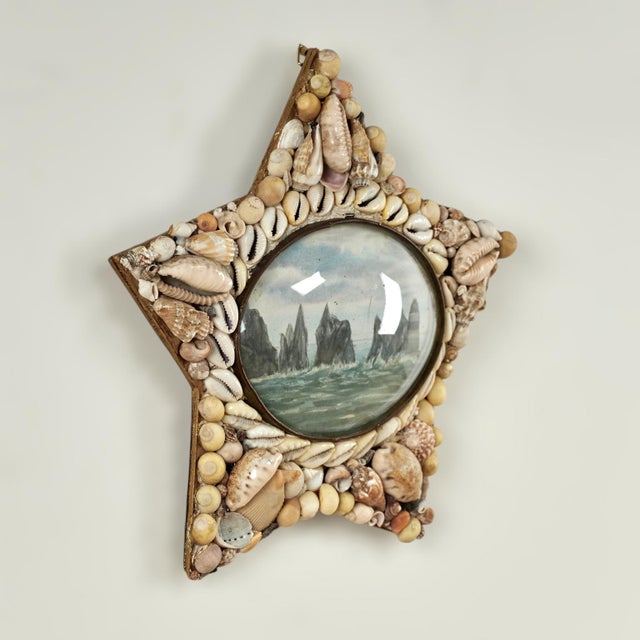 Charming antique sailors valentine handcrafted in exotic seashells in a star form with a rocky coastline image under a...