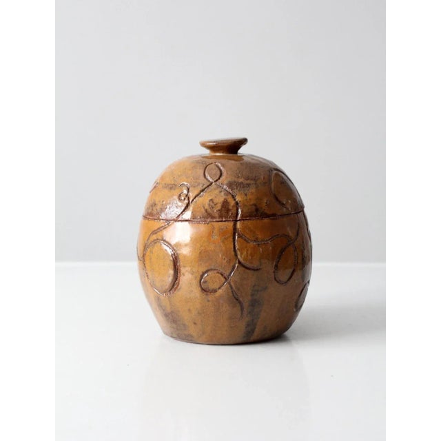 A vintage studio pottery jar signed by artist S. Miller, featuring a rounded, bulbous form, a tawny-brown glaze, and an...