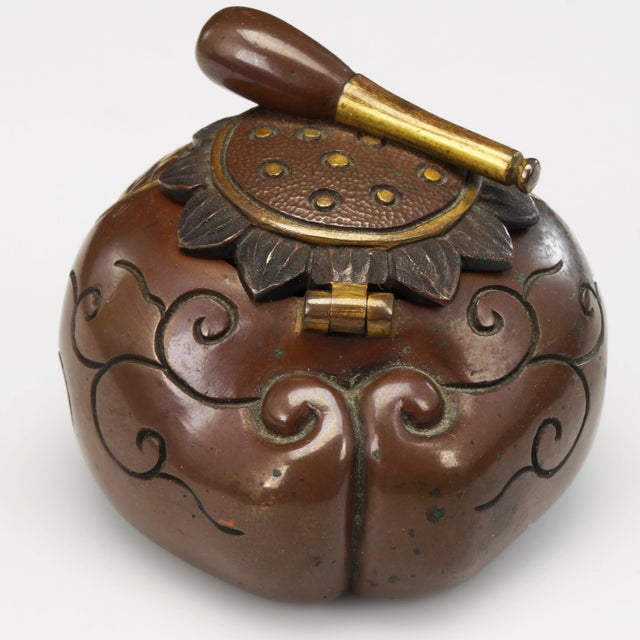 A small inkwell with a globular body and a lid shaped like a Buddhist mokugyo drum and beater. The heavy copper body has...