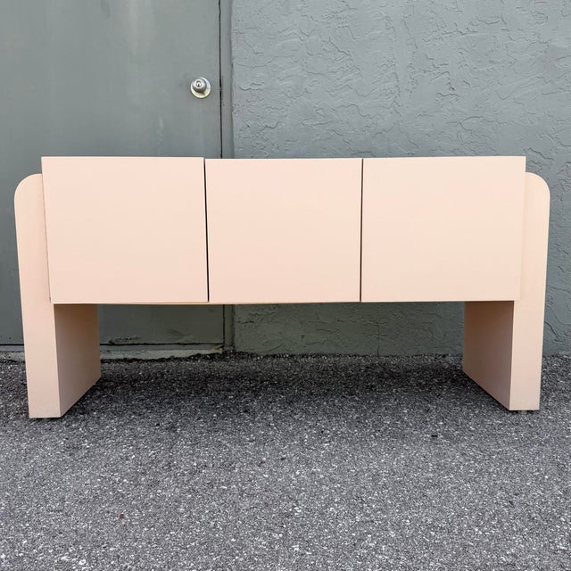 Striking vintage credenza featuring a soft blush pink laminate finish and bold Art Deco Revival styling. The streamlined...