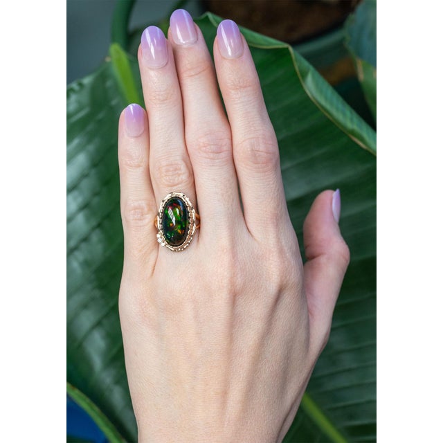 A bold 8.6 carat black opal takes center stage, flashing vivid play-of-color with every movement, framed by natural...
