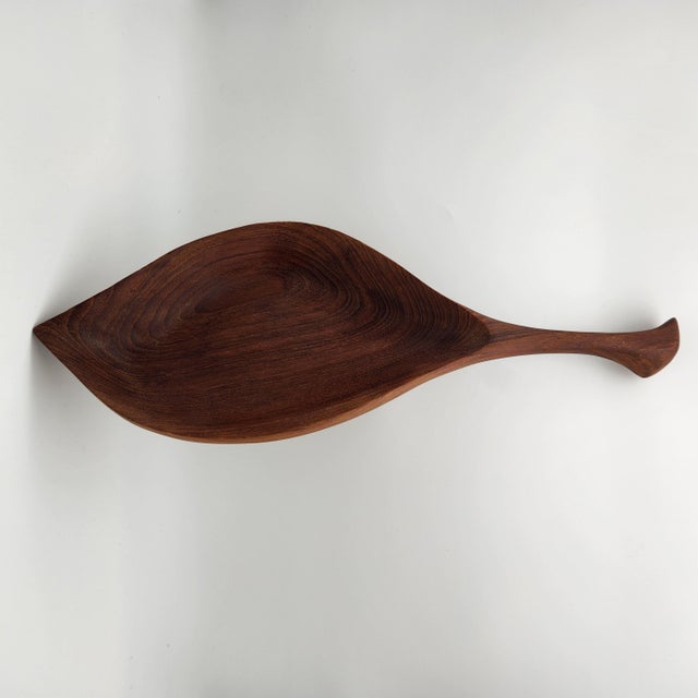 Hand-carved teak leaf-shaped bowl with sculptural stem handle and rich visible grain, mid-century modern style of Emil Milan