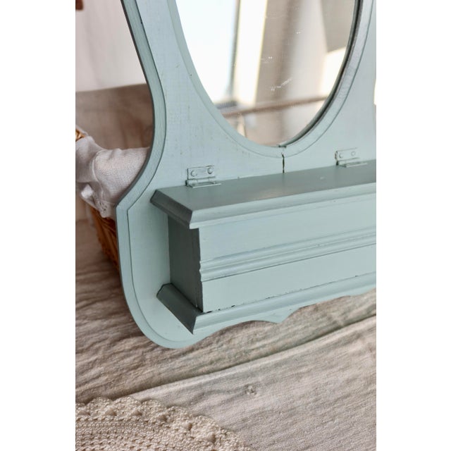 Antique entryway mirror in solid wood, painted a pale blue, with a small built-in storage compartment at the bottom. Its...