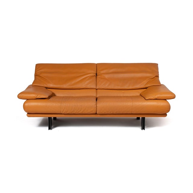 Four black lacquered steel legs intersect beneath a low base; seat and back cushions are upholstered in cognac leather,...