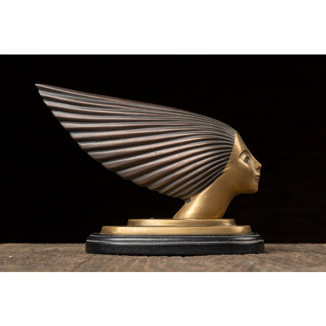 A striking Art Deco hood ornament known as Spirit of the Wind, featuring a stylized female figure with swept-back,...
