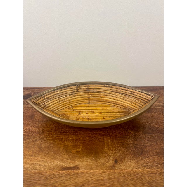 Sculptural vintage rattan bowl featuring an unusual elongated, boat-shaped silhouette with beautifully aged solid brass...