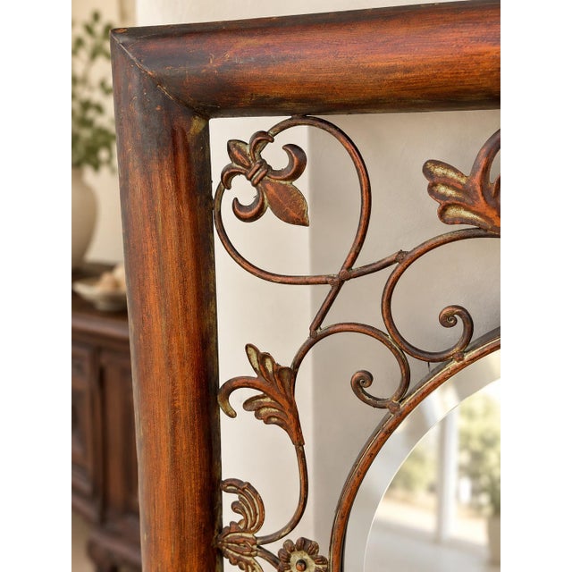 A richly decorative vintage wall mirror featuring a circular beveled mirror inset within an architectural square metal...
