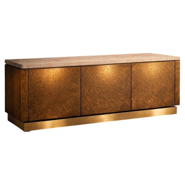 This elegant sideboard is defined by its striking façade in hand-hammered brass, featuring three doors with a richly...