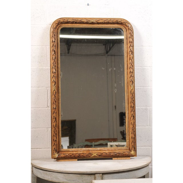 An elegant antique Louis Philippe mirror featuring a richly carved giltwood frame with an exquisite trailing garland and...