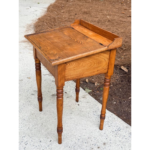 Antique writing desk made of chestnut in a medium wood tone. It features a hinged, slanted top that reveals a storage...