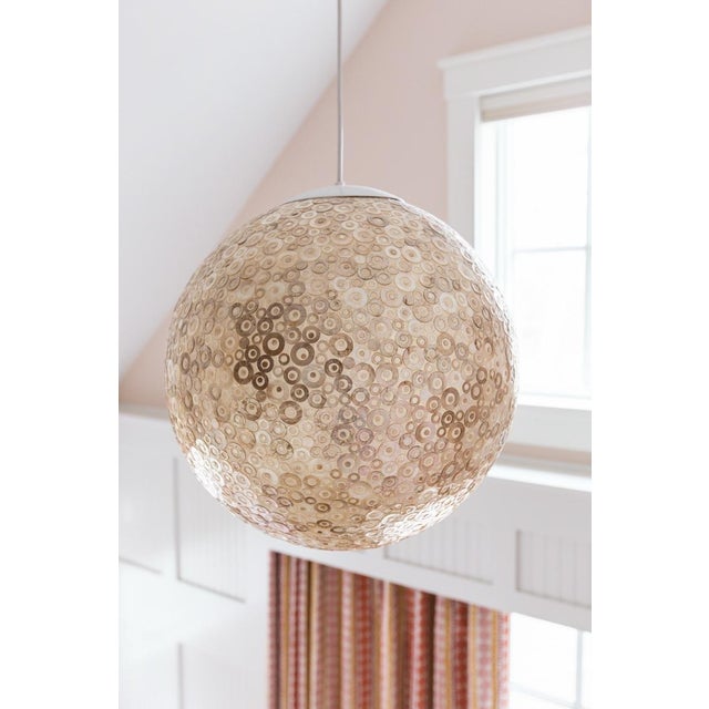 The light fixture in the image is a globe-shaped pendant light featuring a textured surface made of circular patterns,...