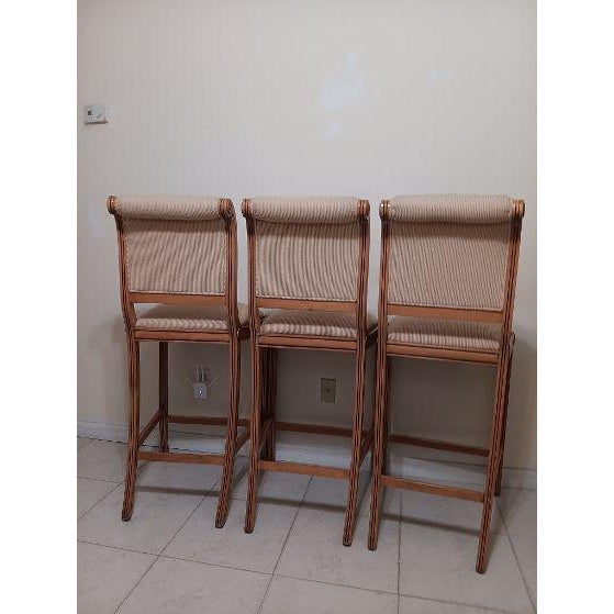 Three wooden counter-height stools with striped upholstered seats and backrests Style: Traditional Color: Beige...