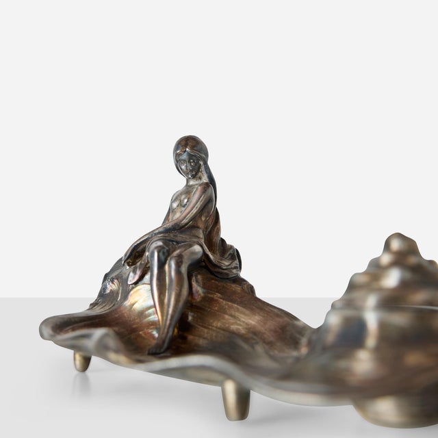 Elongated wave-form base with classical draped figure reclining against rolling sea at one end. Hinged inkwell compartment...
