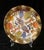 This is a decorative fused art glass plate featuring a stylized still-life motif of birds, fruits and foliage in earth...