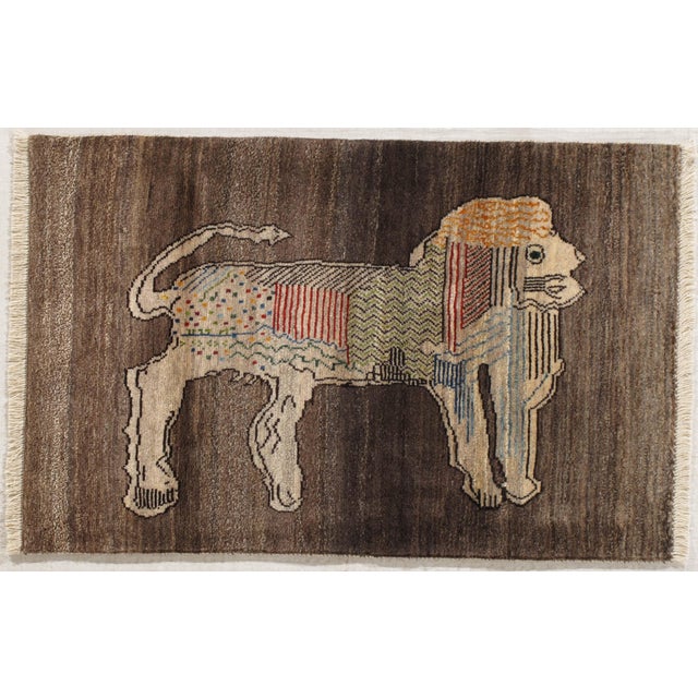 Hand-knotted Persian Gabbeh wool rug featuring a stylized lion motif on a red field, framed by a border of small...