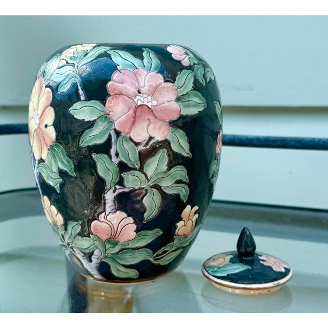 Gorgeous hand-painted porcelain temple jar with lid. The backdrop is a deep green, almost black shade. The perfect...