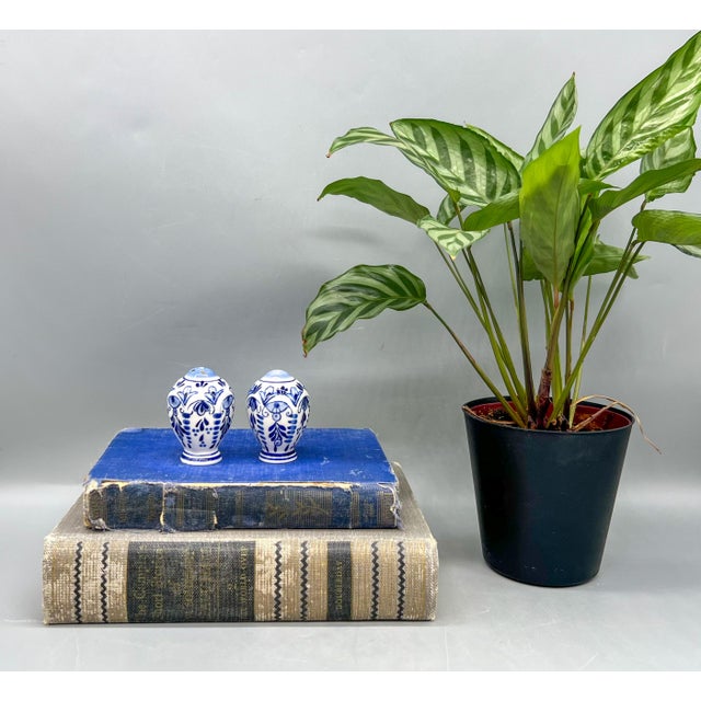 Exquisite pair of ceramic salt and pepper shakers with hand-painted cobalt blue floral and scroll motifs on white. One has...