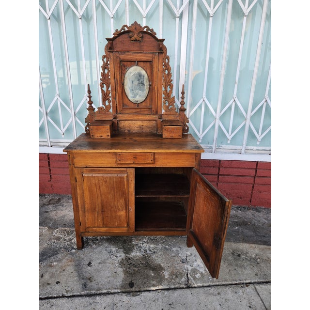 Hand-carved wooden vanity is constructed from solid wood with a natural brown finish. This piece has an ornate top section...