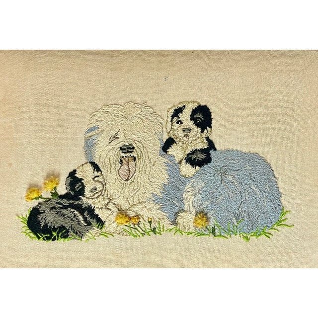 A well-executed needlework on linen depicting an old english sheepdog with her two puppies among the meadows and flowers....