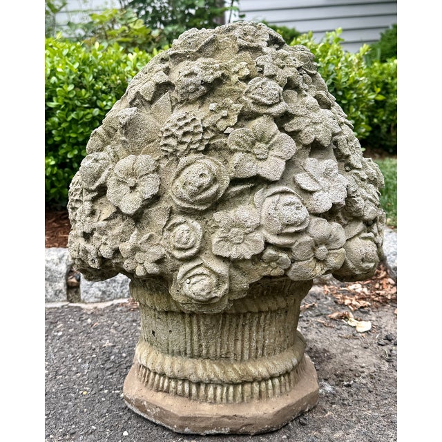 A cast stone floral basket garden ornament, featuring an abundant arrangement of molded roses, blossoms, leaves, and...