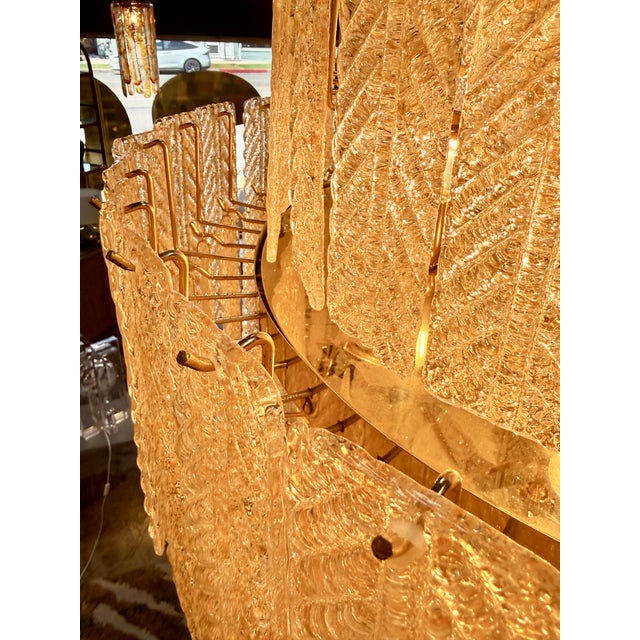 Striking statement chandelier featuring cascading tiers of amber-toned textured glass panels with an elegant leaf and...
