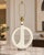 Table lamp with a glossy ivory-white ceramic body in an open-loop shape, with a central ribbed detail and brass-tone...