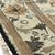 A 9' x 12' hand-knotted wool rug with an ivory field with an allover pattern of olive and tan flowers and leaves inside a...