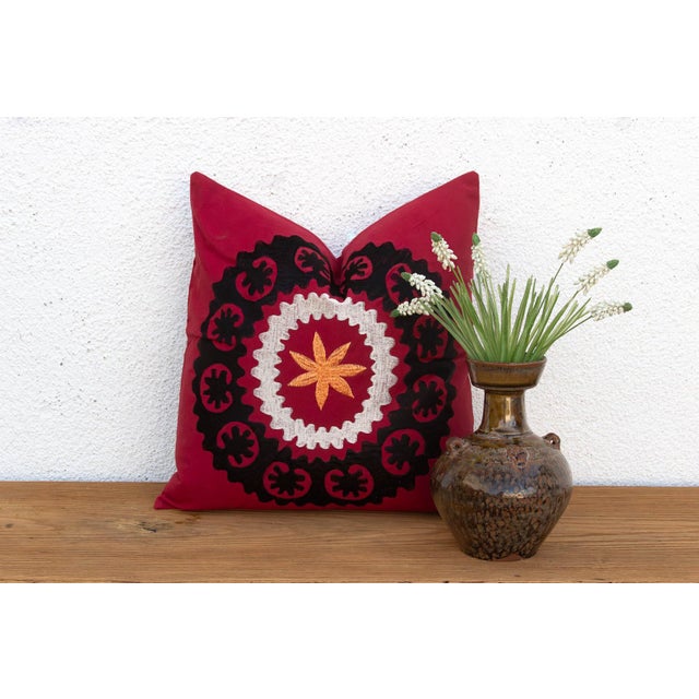 A bold black scalloped medallion anchors this pillow — a wine-red ground framing a cream ric-rac ring and a radiating...