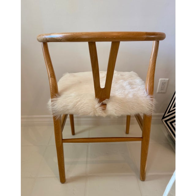 Pair of Wishbone Armchairs with custom goatskin seats. Each chair features a heavy, solid oak wood framework finished in a...