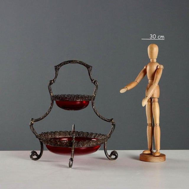 Two-tier stand in embossed, pierced, and chiseled silver with leafy scrolls. Garnet red cut glass bowls. Silver hallmarks...