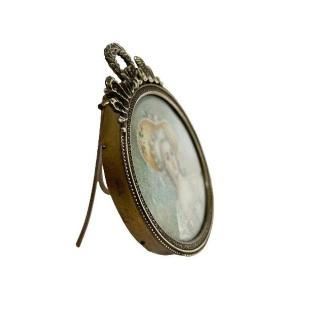 A 19th century bronze miniature portrait frame. A French oval hand-painted portrait of a lady in a bronze frame, behind...