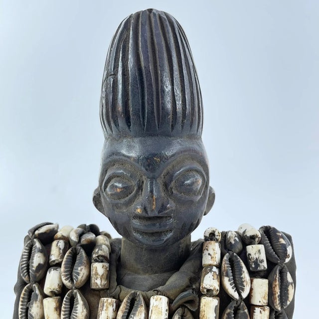 This figure is adorned in a cowrie shell vest, which is removable, and on a custom base. Ibeji figures, carved by the...