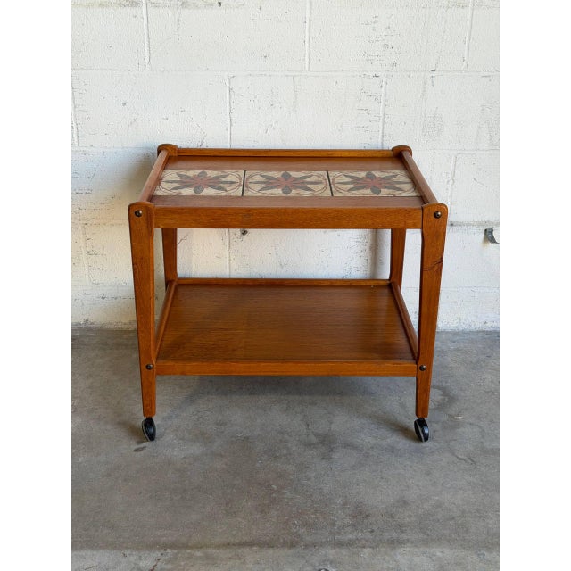 This two-tier mobile cart features an upper shelf with ceramic tiles and a lower wooden tier. Smooth rolling casters...