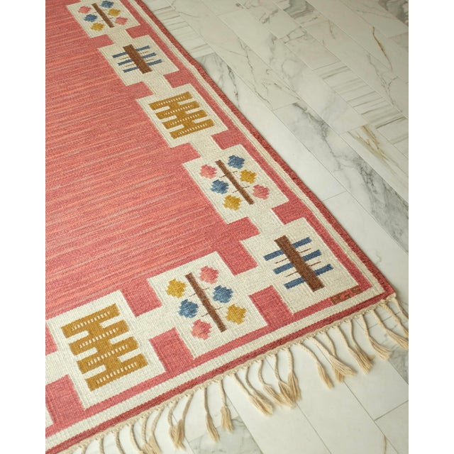Vintage Swedish Kilim rug by Swedish textile designer Anna Greta Sjöqvist. Beautiful pink/red base with a geometric...