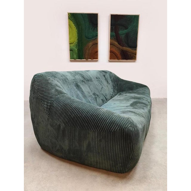 This vintage lounge sofa from the 1970s is upholstered in a deep green-tinted corduroy and features a soft, organic...