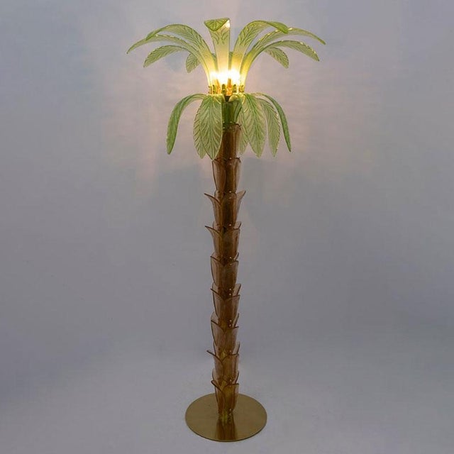 The floor lamp which reproduces the trunk and leaves of a palm tree with pieces of glass is composed of a circular base...