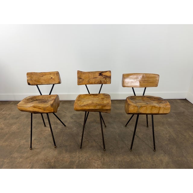 A striking set of three sculptural dining or accent chairs crafted from thick hand-carved solid wood with blackened iron...