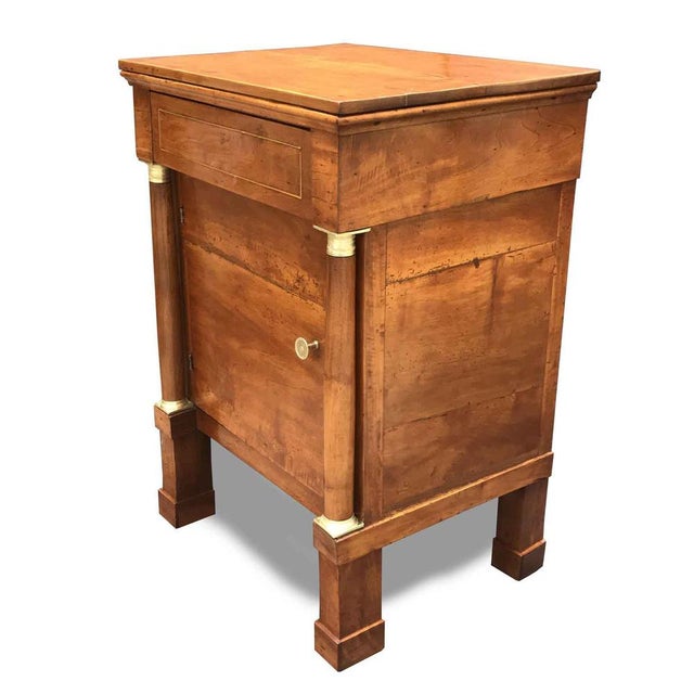 Antique Empire Walnut Nightstand: An Empire nightstand of French origin, featuring an elegantly trimmed brass drawer atop...