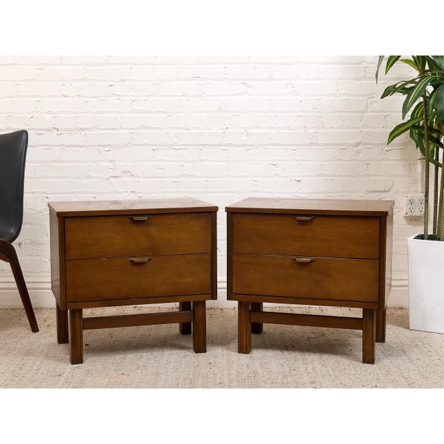 A handsome matching pair of vintage Mid-Century Modern nightstands featuring warm walnut-toned wood, two spacious drawers,...