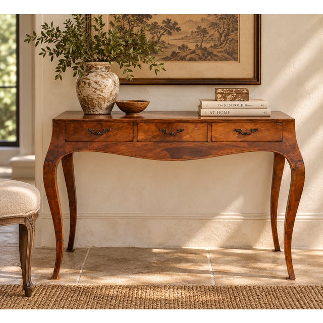 A slim Italian writing table in walnut, with a top and apron veneered in swirling, figured grain that looks like flowing...
