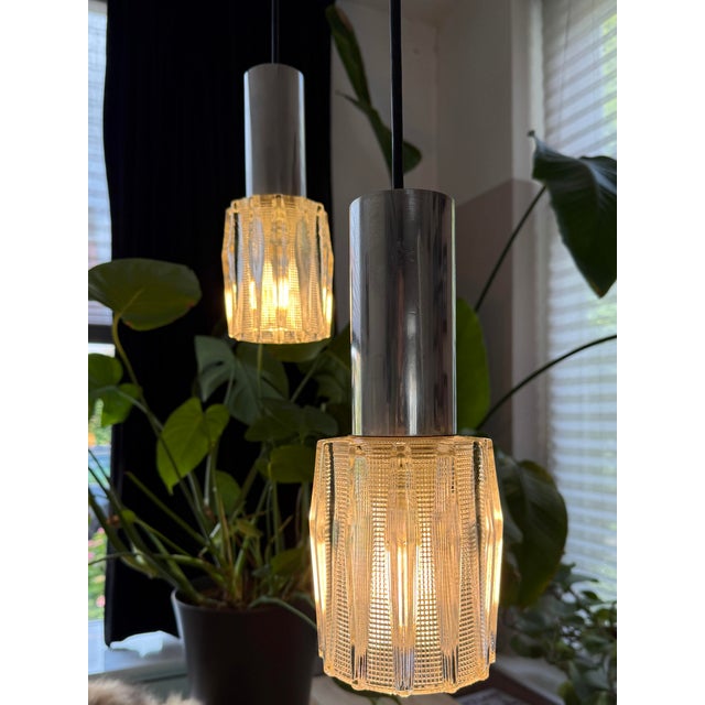 This pair of pendant lights combines textured pressed glass shades with polished chrome-plated cylindrical fittings in a...