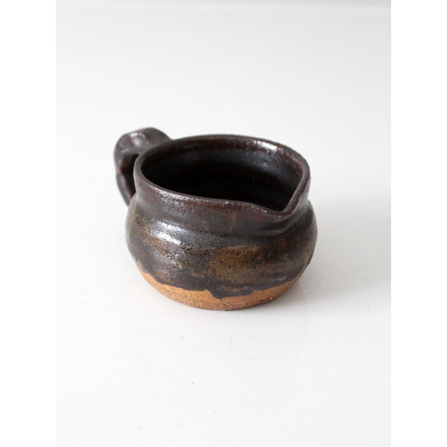 This vintage studio pottery creamer features a hand-shaped form with a deep brown dipped glaze that flows naturally into a...