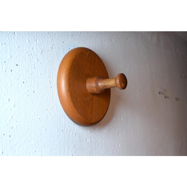 This is a beautifully designed wall hook made of teak wood with a distinctive, saucer-shaped backplate. The backplate is...
