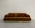 A dramatic sculptural sofa featuring oversized rolled arms, deep tufting, and a low-profile silhouette anchored by a...