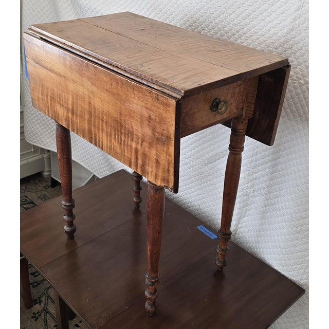 A finely figured early 19th-century American drop-leaf table crafted in solid tiger (curly) maple, featuring a single...